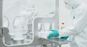 Operator handling ready-to-use containers beside robotic equipment in an aseptic pharmaceutical fill-finish system.